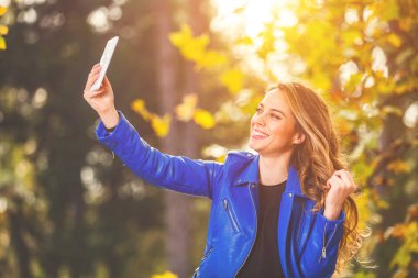 Park sezon sonbahar renkleri ile Smartphone kullanarak sevimli genç kadın.