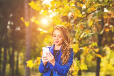 Park sezon sonbahar renkleri ile Smartphone kullanarak sevimli genç kadın.