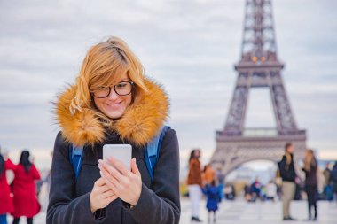 Paris geçmişi ve Eyfel kulesi olan cep telefonu kullanan bir kız..