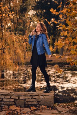 Sevimli kız Park sonbahar renkleri ile cep telefonu kullanarak.