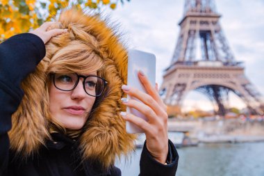 Paris geçmişi ve Eyfel kulesi olan cep telefonu kullanan bir kız..