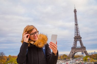 Paris geçmişi ve Eyfel kulesi olan cep telefonu kullanan bir kız..