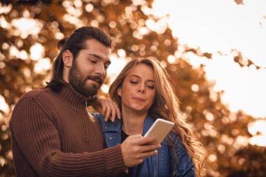 Genç çift sonbahar renkli park'cep telefonu kullanma.