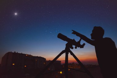 Kentsel ortamda astronomik teleskop ile gökyüzüne bakan genç adam.