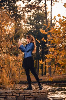 Sevimli kız Park sonbahar renkleri ile cep telefonu kullanarak.