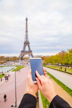 Paris geçmişi ve Eyfel kulesi olan cep telefonu kullanan bir kız..