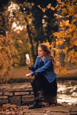 Sevimli kız Park sonbahar renkleri ile cep telefonu kullanarak.