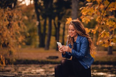 Sevimli kız Park sonbahar renkleri ile cep telefonu kullanarak.
