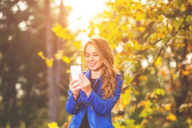 Park sezon sonbahar renkleri ile Smartphone kullanarak sevimli genç kadın.