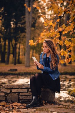 Sevimli kız Park sonbahar renkleri ile cep telefonu kullanarak.