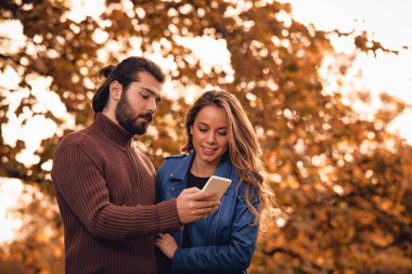 Genç çift sonbahar renkli park'cep telefonu kullanma.