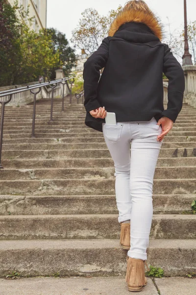 Woman walking up the stairs and taking / putting cellphone from / in the pocket.