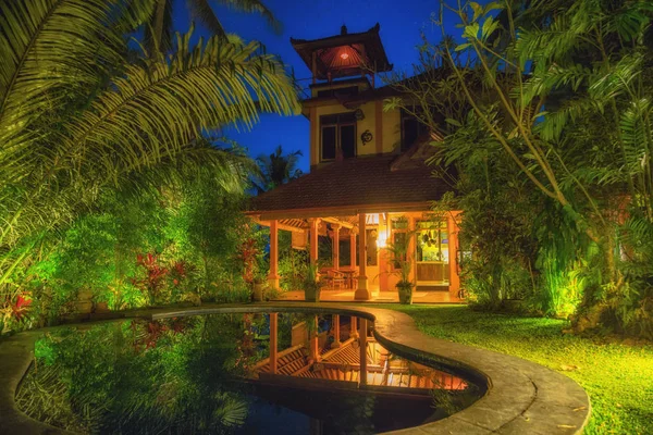 在巴厘岛度假村的房子与池塘和树木在夜间时间 — 图库照片