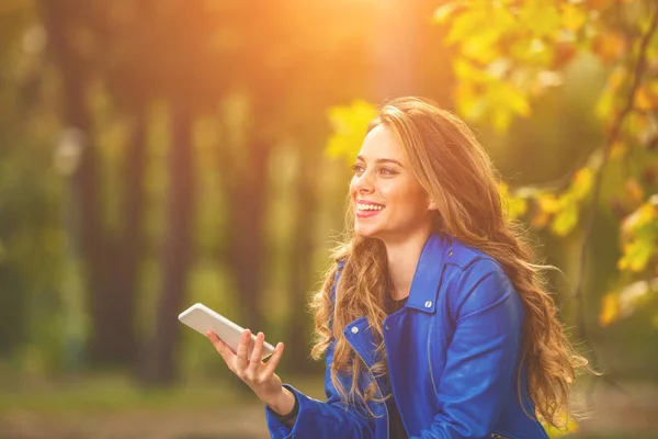 かわいい若い女性公園秋のシーズン カラーでスマート フォンを使用して — ストック写真