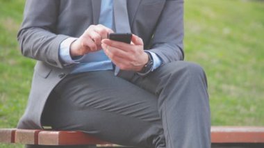 Açık bankta oturan smartphone kullanarak iş adamı