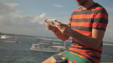 Sakallı adam çizgili tişört deniz kenarında smartphone kullanarak