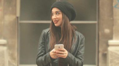 Genç esmer kadın smartphone kullanarak kırmızı ruj ve bere şapka ile şehir arka plan bulanık