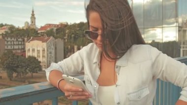 Genç kadın güneş gözlüğü manifatura köprüde smartphone kullanarak arkadaşlar