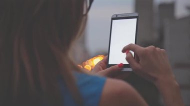 Akşam bulanık şehir arka plan üzerinde smartphone kullanarak gözlüklü genç kadın