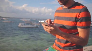Sakallı adam çizgili tişört deniz kenarında smartphone kullanarak