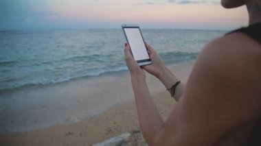 Deniz kenarında oturan smartphone kullanan kadın