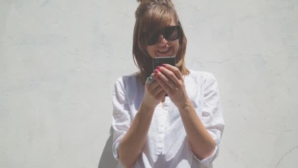 Mulher Com Pão Cabelo Óculos Usando Smartphone Fundo Parede Branca — Vídeo de Stock