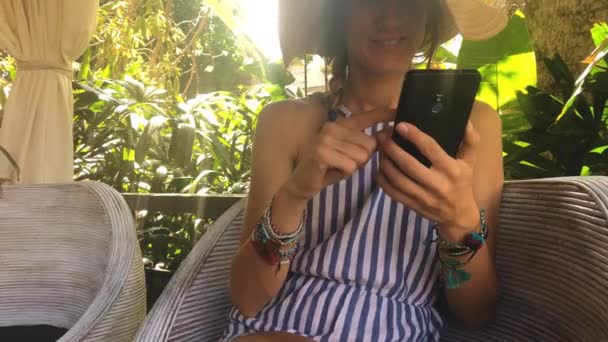 Giovane Donna Abito Cappello Sms Agli Amici Utilizzando Smartphone Seduto — Video Stock