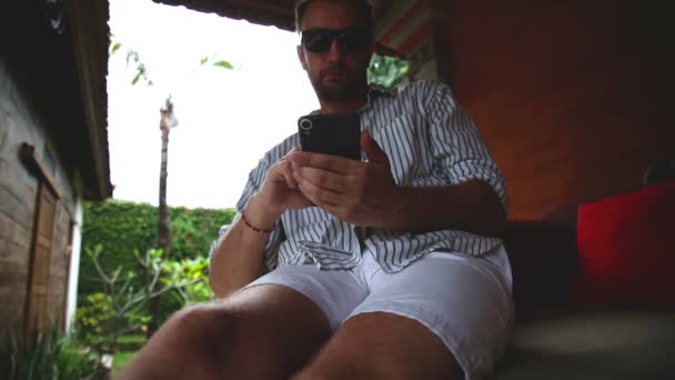 Άνθρωπος Που Κάθεται Στον Καναπέ Βεράντα Χρησιμοποιώντας Smartphone — Αρχείο Βίντεο