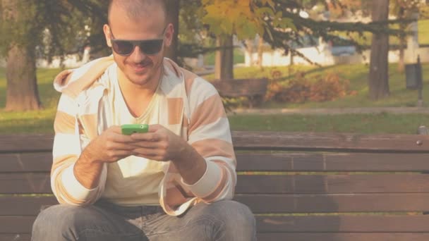 在公园里 男子使用智能手机坐在长椅上 — 图库视频影像
