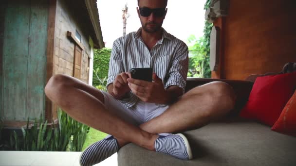 Άνθρωπος Που Κάθεται Στον Καναπέ Βεράντα Χρησιμοποιώντας Smartphone — Αρχείο Βίντεο