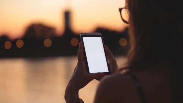 Jeune femme en lunettes utilisant un smartphone en soirée sur fond de ville floue 