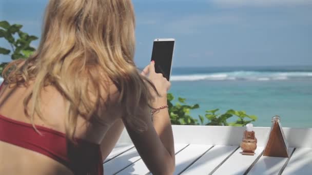 女性が海でテーブルに座っているスマート フォンを使用して — ストック動画