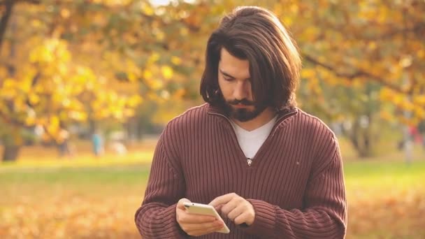 Γενειοφόρος Άνδρας Μακριά Μαλλιά Χρησιμοποιώντας Smartphone Στο Φθινοπωρινό Πάρκο — Αρχείο Βίντεο