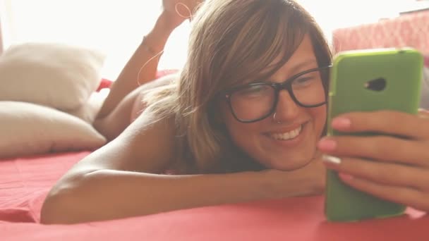 Yatakta Döşeme Smartphone Kullanarak Gözlük Güzel Kadın — Stok video
