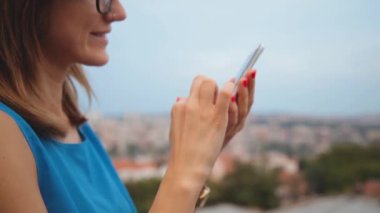 Akşam bulanık şehir arka plan üzerinde smartphone kullanarak gözlüklü genç kadın