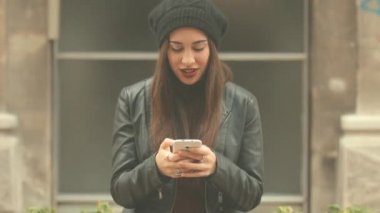 Genç esmer kadın smartphone kullanarak kırmızı ruj ve bere şapka ile şehir arka plan bulanık