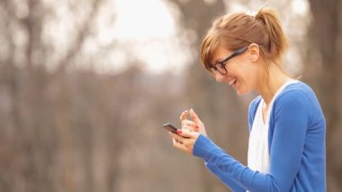 Mavi bluz ve kot sonbahar parkta smartphone kullanarak güzel kadın