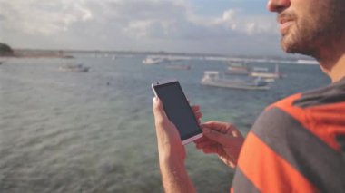 Sakallı adam çizgili tişört deniz kenarında smartphone kullanarak