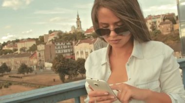 Genç kadın güneş gözlüğü manifatura köprüde smartphone kullanarak arkadaşlar