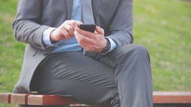 Açık bankta oturan smartphone kullanarak iş adamı