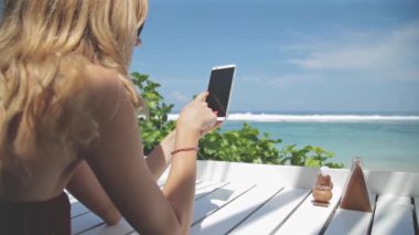 Deniz tarafından masada oturan smartphone kullanan kadın