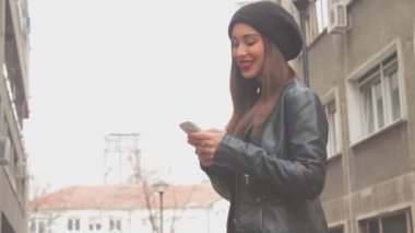Genç esmer kadın smartphone kullanarak kırmızı ruj ve bere şapka ile şehir arka plan bulanık