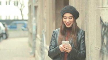 Genç esmer kadın smartphone kullanarak kırmızı ruj ve bere şapka ile şehir arka plan bulanık