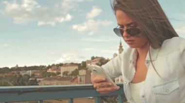 Genç kadın güneş gözlüğü manifatura köprüde smartphone kullanarak arkadaşlar