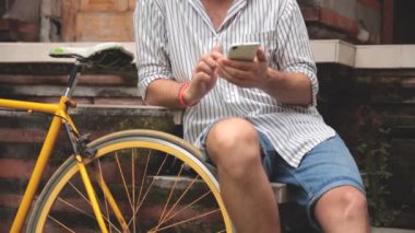 Genç adam bisiklet oturan Asya bahçesinde Smartphone kullanarak