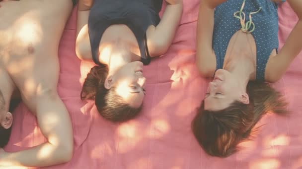 Zwei Frauen Und Ein Mann Liegen Auf Einer Rosa Decke — Stockvideo