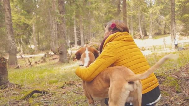 春の森でリラックスした犬をなでる黄色のコートの女 — ストック動画