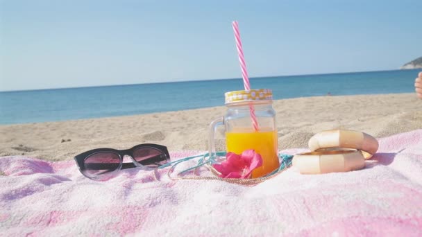 带太阳镜的粉红色毛巾 玻璃瓶中的果汁 手镯和鲜花 度假理念 — 图库视频影像