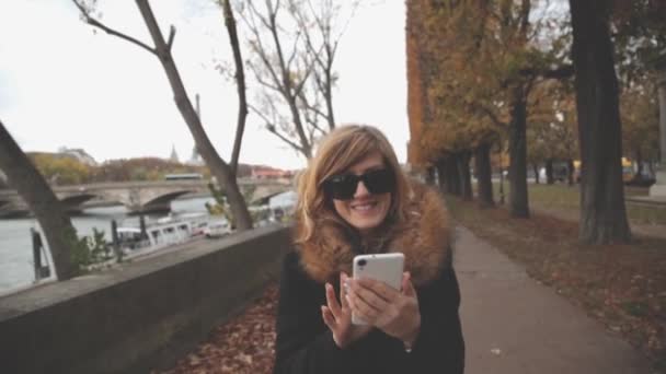若い女性の屋外 スマート フォンを使用してバック グラウンドで川を渡る橋 — ストック動画
