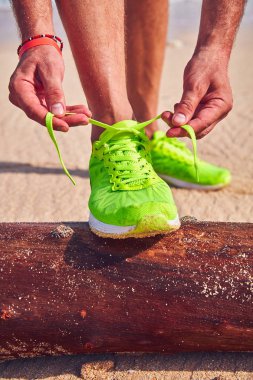 Bir tropikal egzotik plajda çalışan Sneakers bağlama adam.